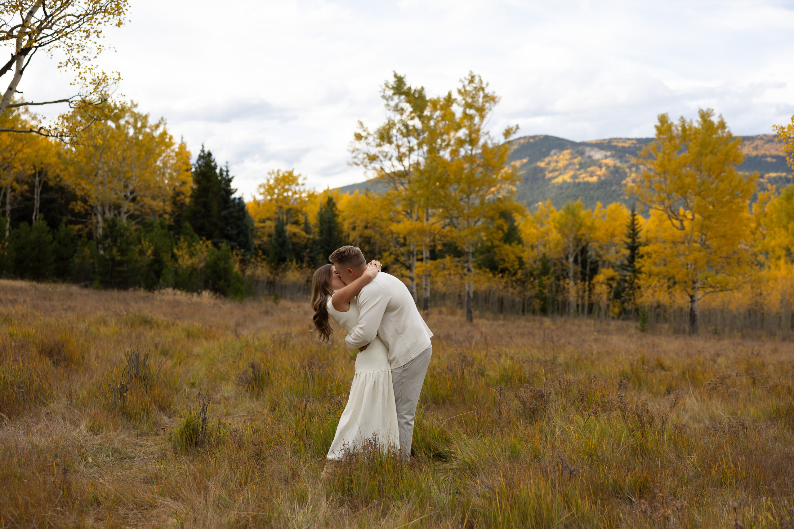 A couple wearing all white kissing during the Fall in the mountains.